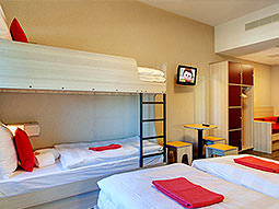 A bunk bed and two single beds in a room with white bedding and red towels on the bed