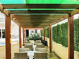 An outdoor seating area with wooden beams above and a swimming pool in the background