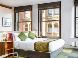 A double bed in a room with large windows and green decor at Roomzzz Manchester City Apartments