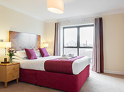 A red double bed next to a bedside table