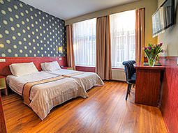 Two single beds in a hotel room with a black polka dot wall, facing a desk, chair and TV on the wall