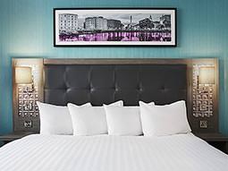 A white double bed in front a blue wall, with a picture above the bed