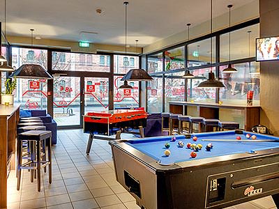 A pool table in the foreground, with table football and bar stools in the background