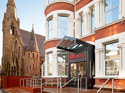 The entrance to Ibis Belfast Queens Quarter, with a grand cathedral in the background, during the day