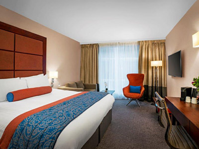 A king room with blue and orange features and a flatscreen TV mounted to the wall at Leonardo Royal Hotel London St Paul's