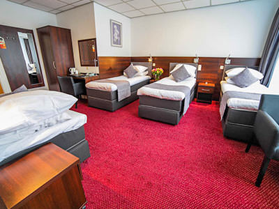 Four single beds in a hotel room, featuring a wardrobe right at the back of the room