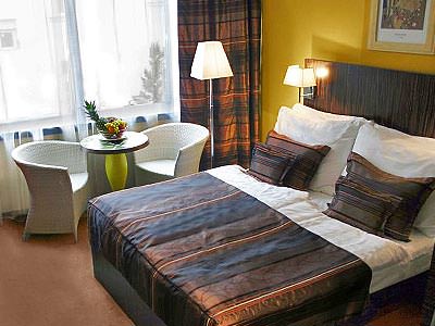 A double bed, topped with a throw and two cushions, with two chairs and a table in the background - Rank #7