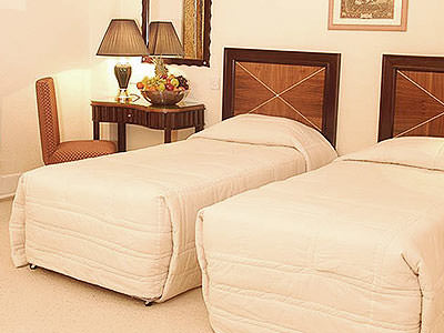 Two single beds in a hotel room, with a bedside table and chair next to one