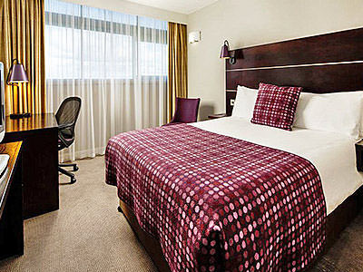 A double bed in a hotel room, with a purple tartan throw and cushion on top 
