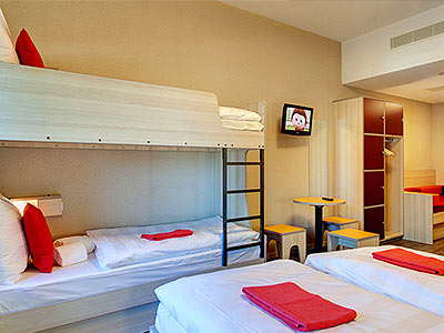 A bunk bed and two single beds in a room with white bedding and red towels on the bed