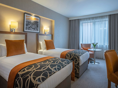 A double bed in a grand hotel room with purple and gold wallpaper, featuring a desk and purple desk chair