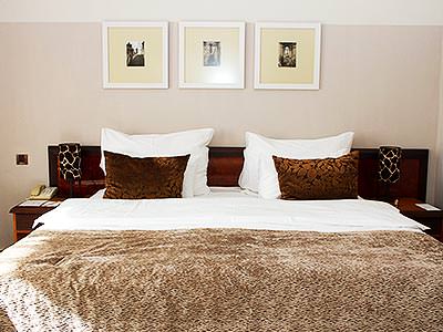 A white double bed with a brown throw and two brown cushions, with three pictures above the bed - Rank #9