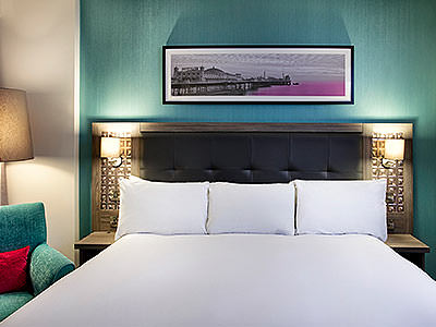 A picture hanging above a white king size bed in a blue hotel room