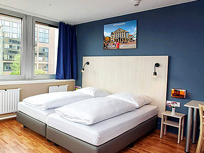 Two single white beds in a blue hotel room, with a bedside table and desk to one side of the bed