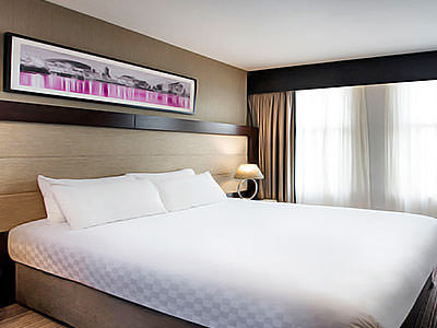 A large double bed with white bedding, in a room with a large black, white and pink landscape canvas on the wall - Rank #4