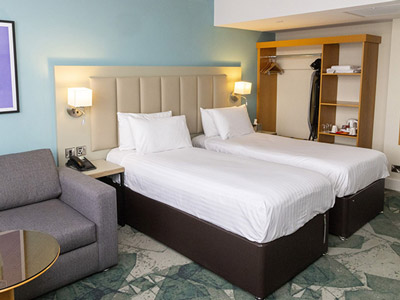 A twin room at Garner Nottingham City Centre with a wardrobe and seating area 