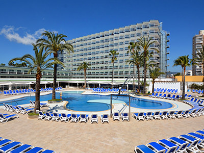 Two double beds with grey bedding, facing a large window, with a desk and chairs in the background