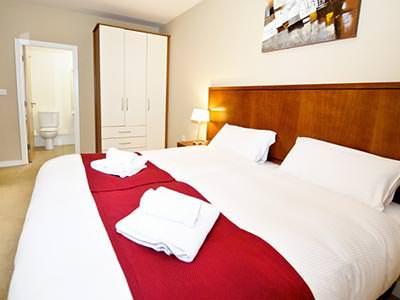 A double bed in a bedroom, with a red runner and wooden headboard