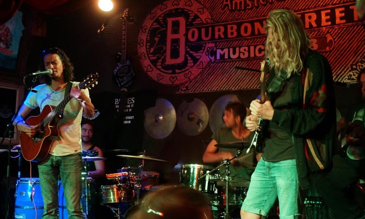 A band playing, a stage with the Bourbon Street logo behind