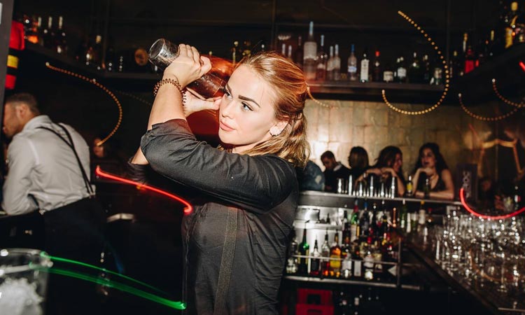 A girl making a cocktail behind a bar