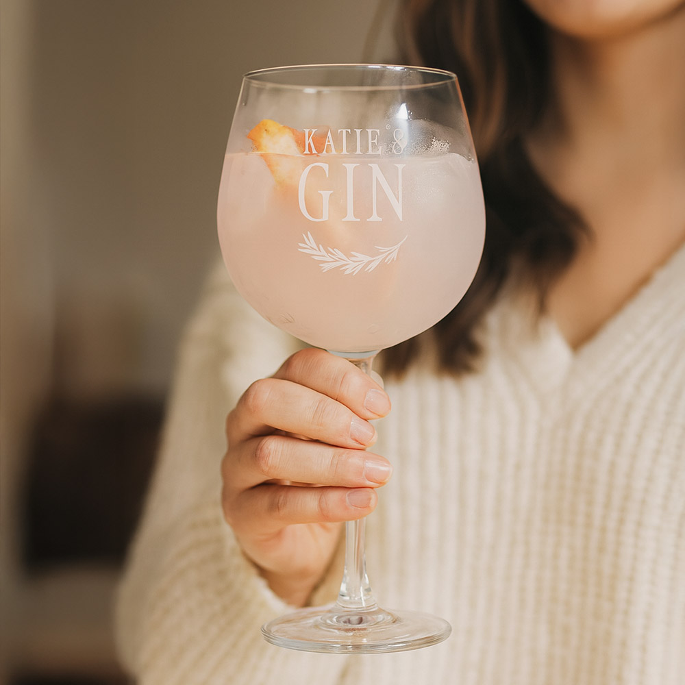 A woman holding a custom gin glass that has been personalised with the custom text Katie's Gin