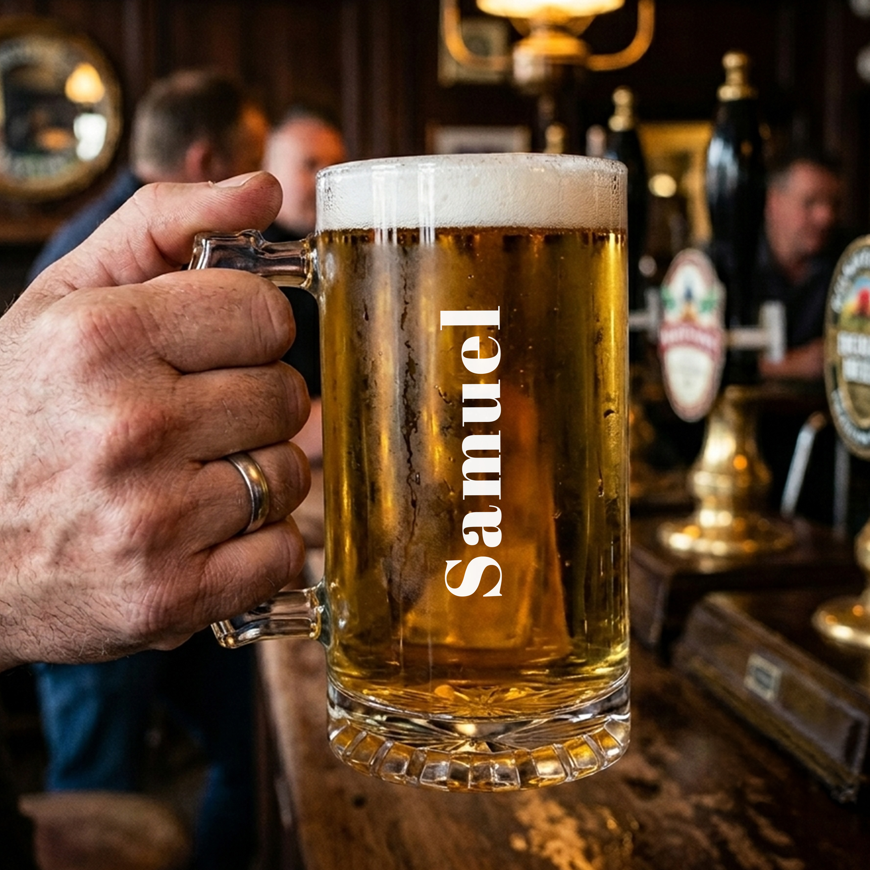 Someone holding a personalised stein in a pub setting with a sturdy glass handle and custom text reading Samuel that runs vertically up the glass