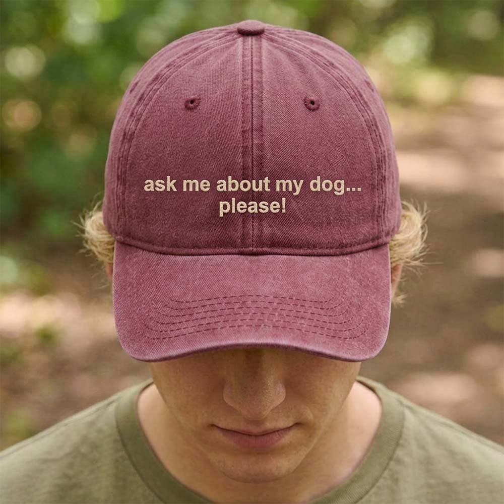 A female model stood in front of an outdoor background wearing a premium cap in red that has been embroidered with the custom phrase ask me about my dog....please! in a tusk font