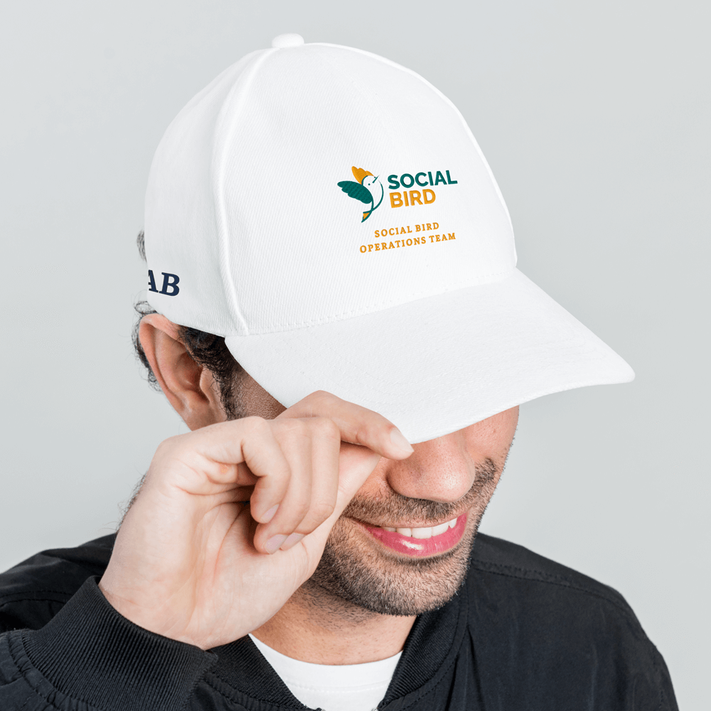 A side view of a male model wearing a white golfing cap with a golf logo embroidered onto it reading social bird, social bird operations team with the initials AB embroidered on the side
