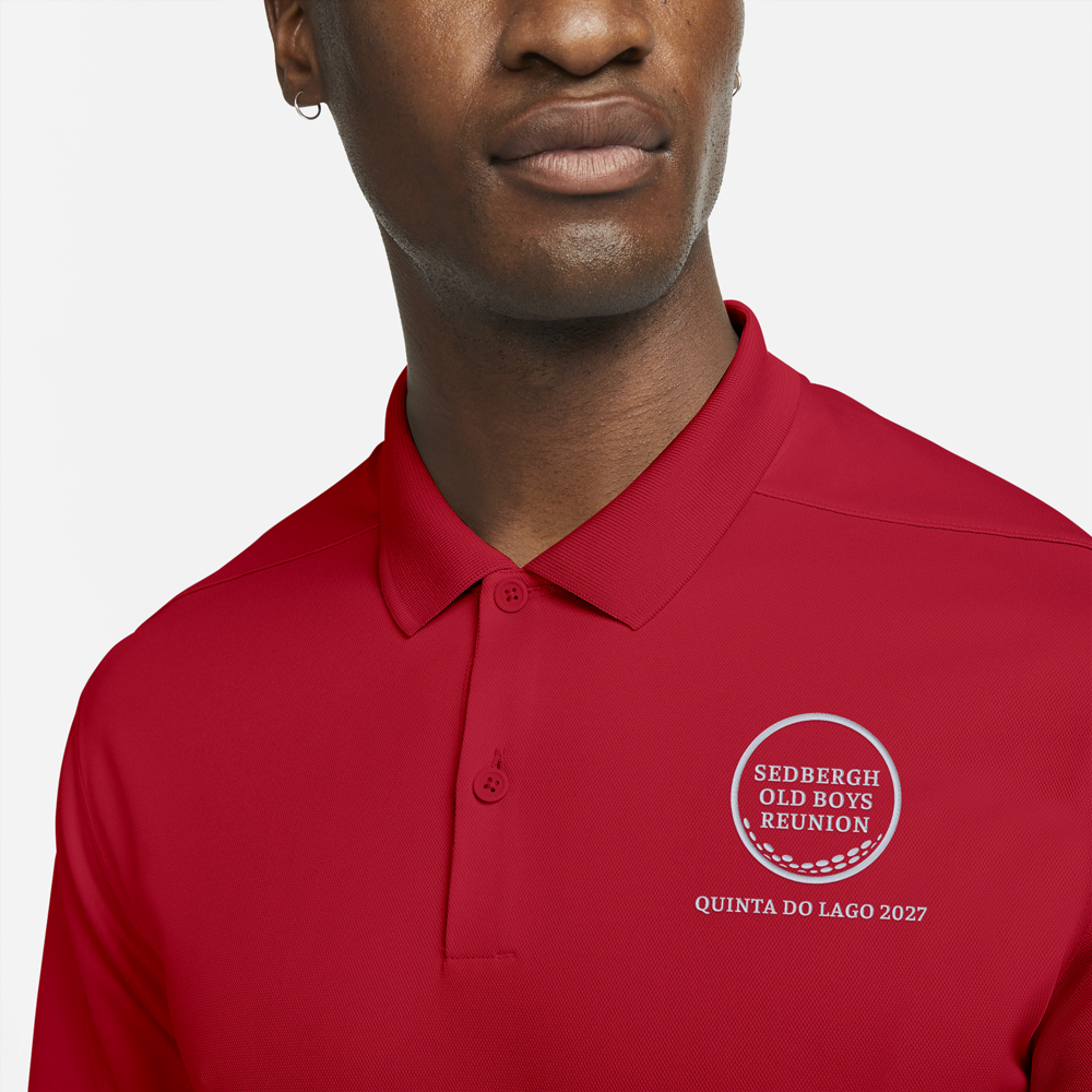 A male model wearing a red custom golf polo with a golf ball design that reads Sedbergh Old Boys Reunion inside the golf ball with Quinta Do Lago 2027 underneath it