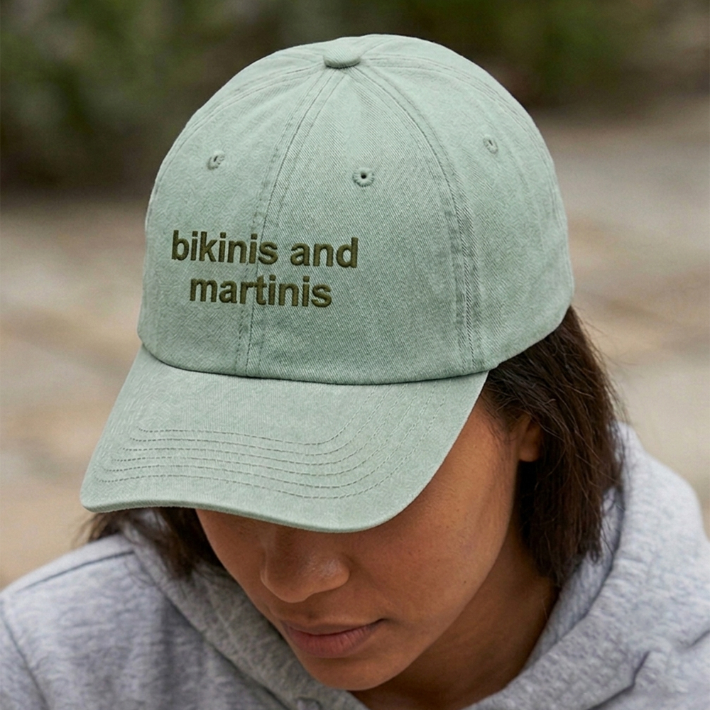 A female model wearing a premium hen do cap in green that has been embroidered with the phrase bikinis and martinis in a darker green font