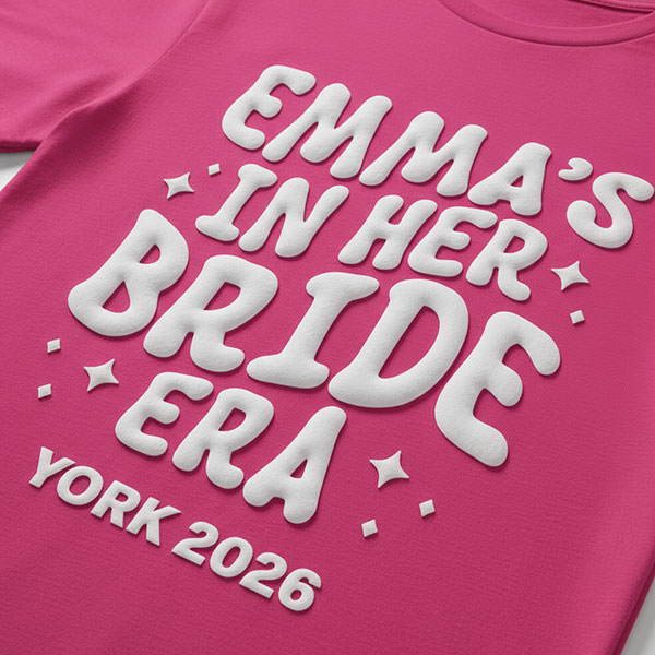 A pink hen do shirt with custom white 'puff print' bubble writing that reads Emma's in her Bride Era, York, 2026
