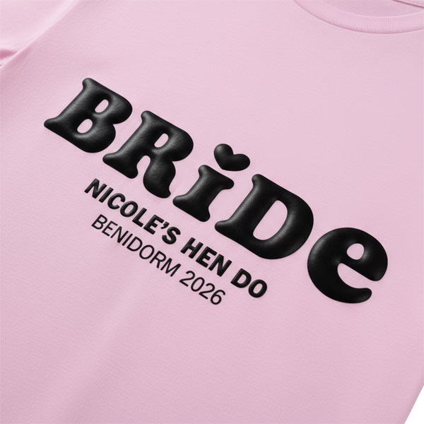 A pink hen do shirt with custom black 'puff print' bubble writing that reads Bride (with a heart above the I) as well as Nicole's Hen Do, Benidorm 2026