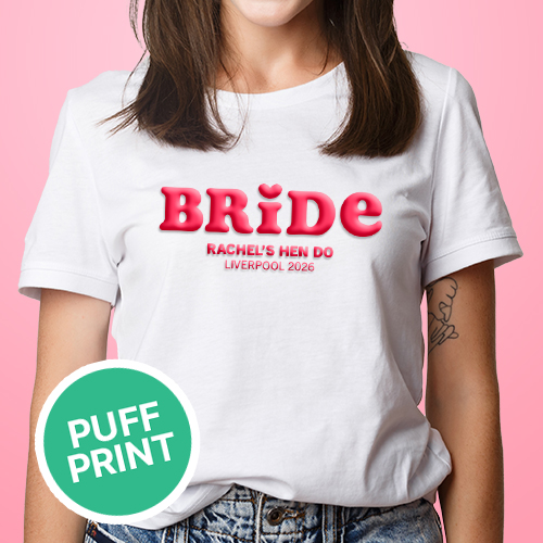 A female model wearing a white hen do shirt with custom pink 'puff print' bubble writing that reads Bride (with a heart above the I) as well as Rachel's Hen Do, Liverpool 2026 
