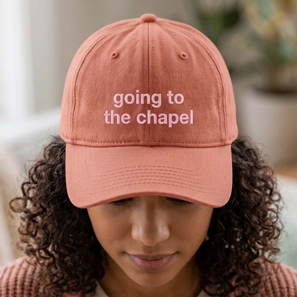 A female model wearing a premium hen do cap in vintage orange with the text going to the chapel embroidered on it in a pink font