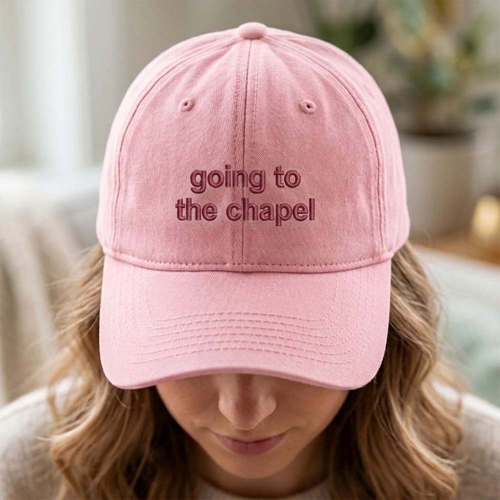 A female model wearing a premium hen do cap in pink with the text going to the chapel embroidered on it in a red font 