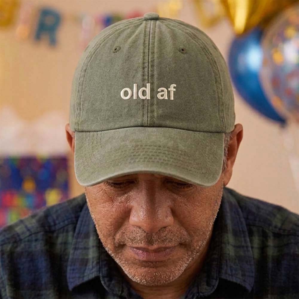A male model stood in front of a blurred birthday background and wearing a premium birthday cap in green that has been embroidered with the phrase old af in a tusk font