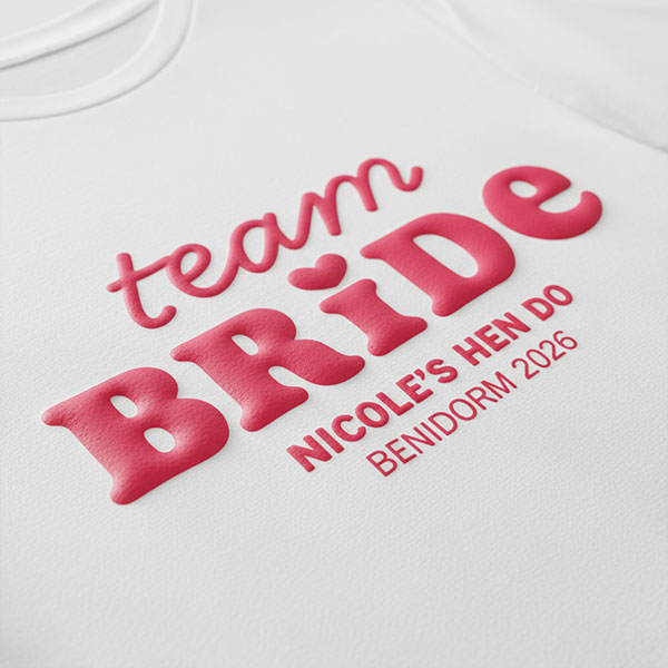 A white hen do shirt with custom pink 'puff print' bubble writing that reads Team Bride, Nicole's Hen Do, Benidorm 2026