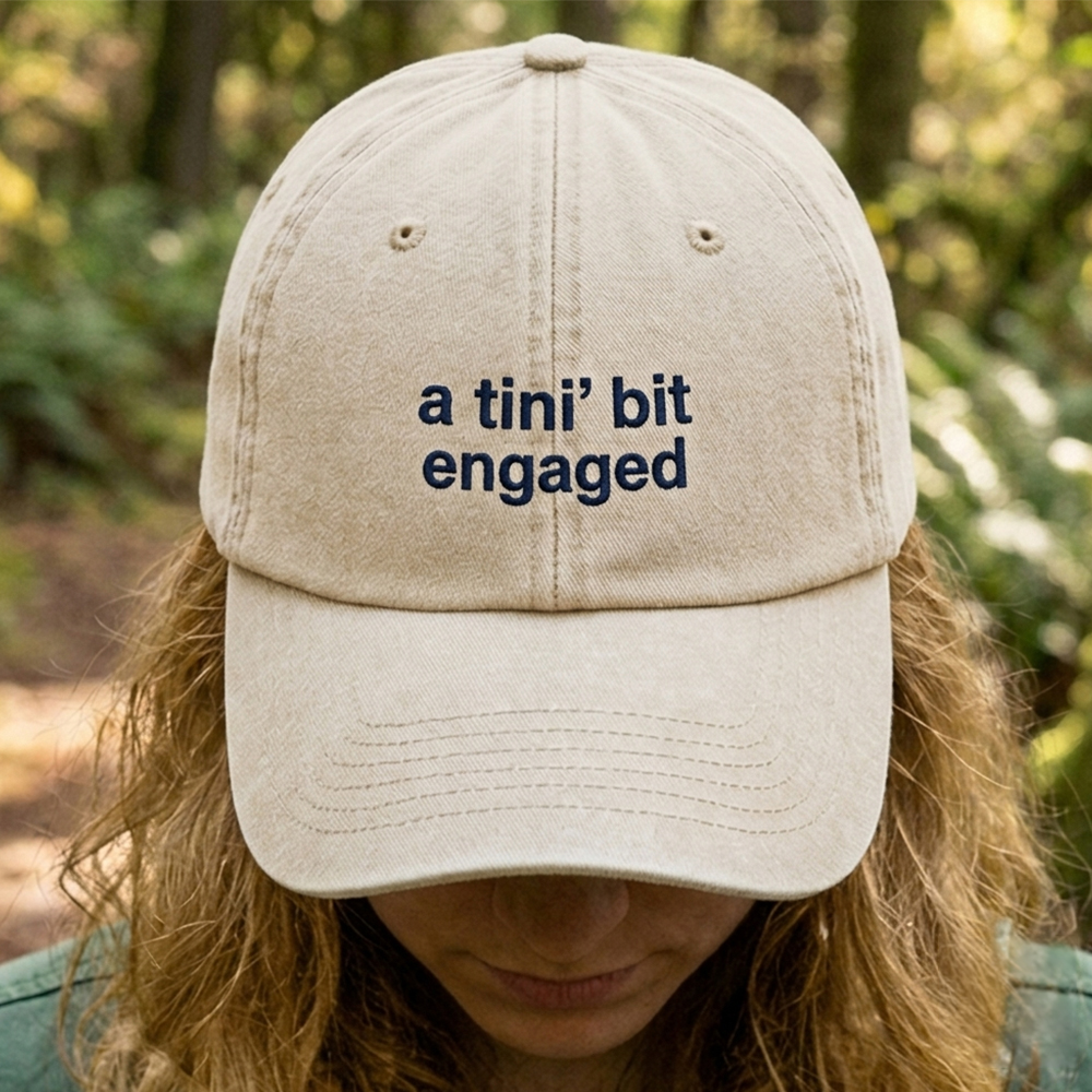 A female model wearing a premium hen do cap in sand that has been embroidered with the phrase a tini bit married in a navy font