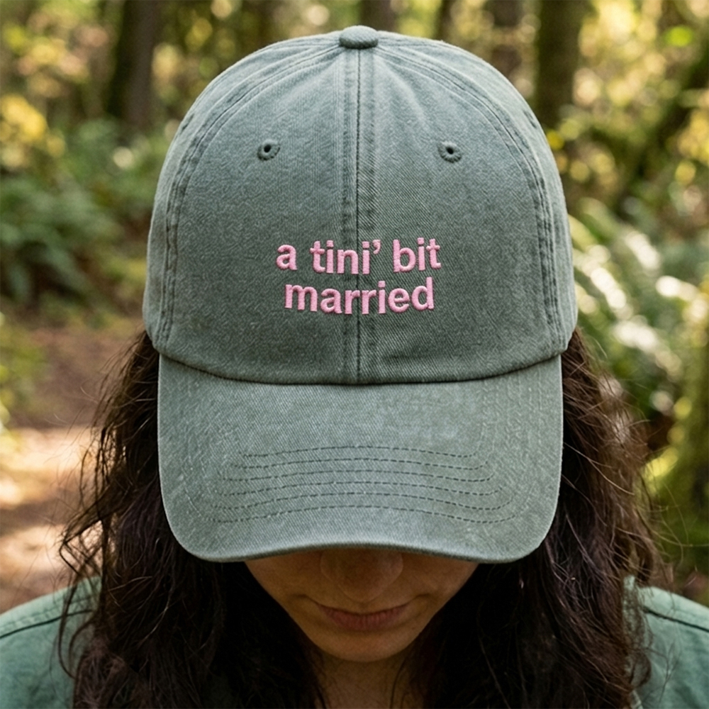 A female model wearing a premium hen do cap in green that has been embroidered with the phrase a tini bit married in a pink font
