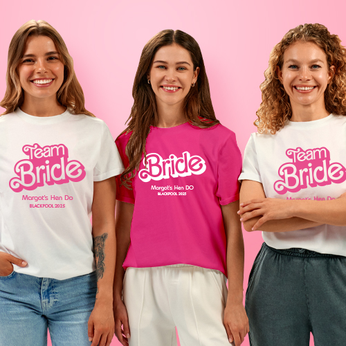 A woman wearing a custom hen do t shirt that reads Bride in the iconic Barbie text with Margot's Hen Do, Blackpool 2026 underneath it whilst her two friends wear t shirts that read Team Bride 