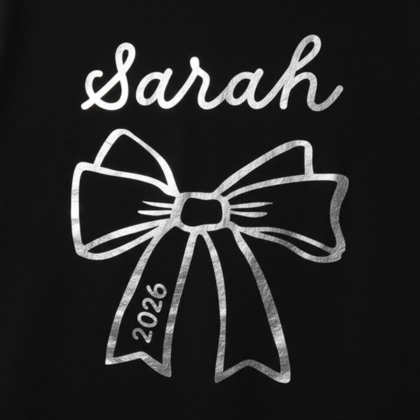 A black hen do shirt with a shiny silver foil bow which has the custom text Sarah above it and 2026 in the bow