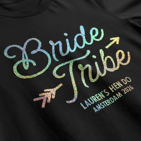A black hen do shirt with custom shiny foil rainbow coloured text that reads Bride Tribe, Lauren's Hen Do, Amsterdam 2026