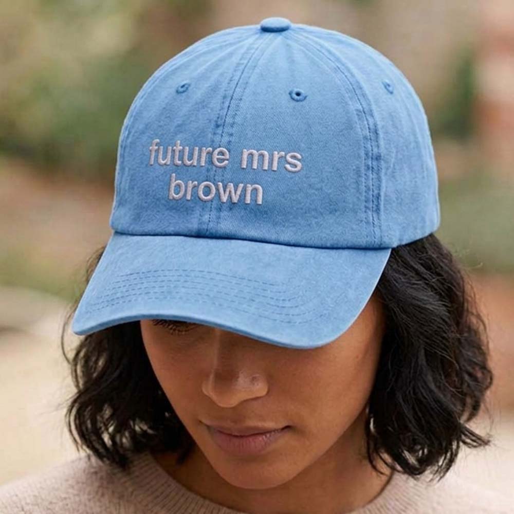 A female model wearing a premium hen do cap in blue with custom text future mrs brown embroidered on it in orchid text