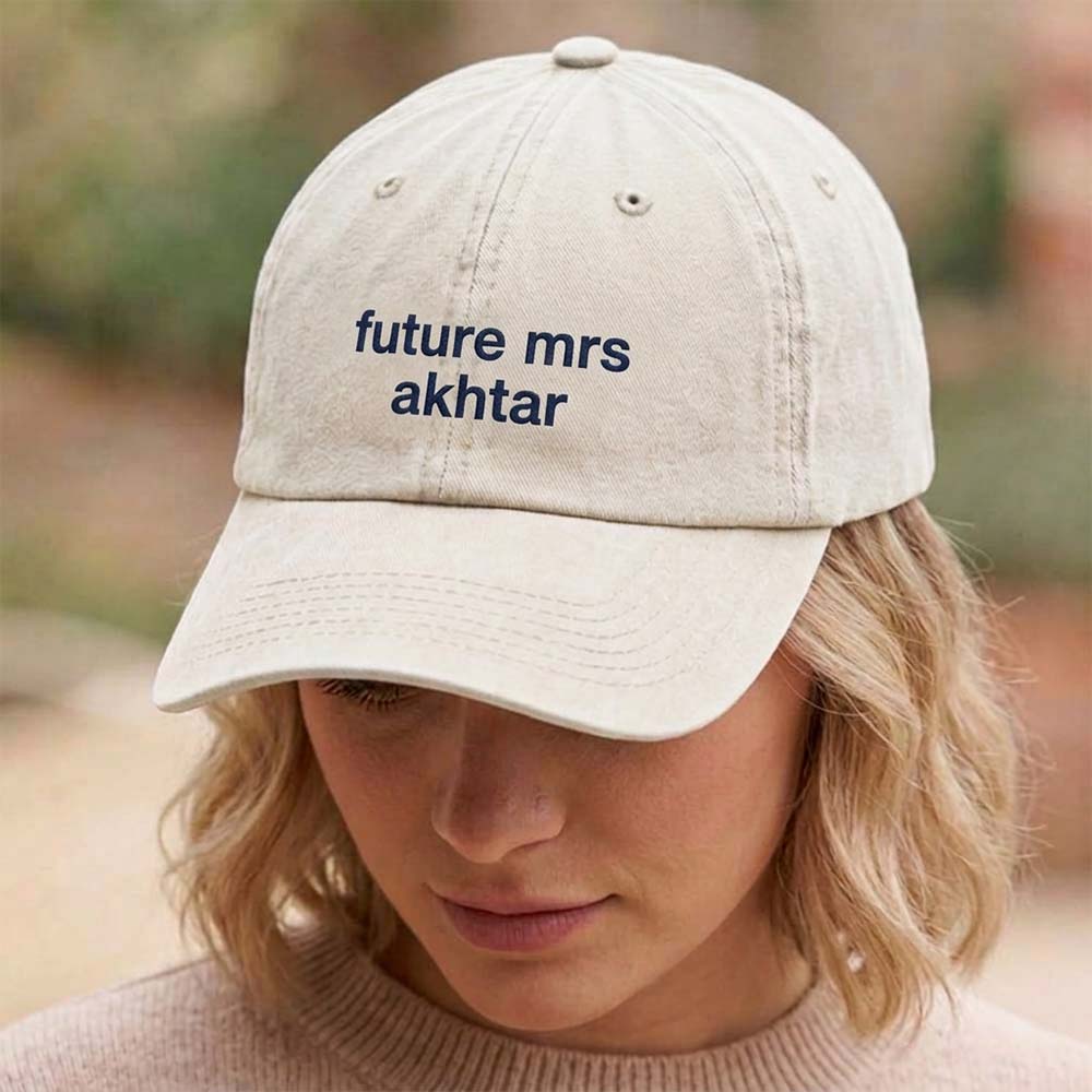A female model wearing a premium hen do cap in vintage sand with custom text future mrs akhtar embroidered on it in navy text