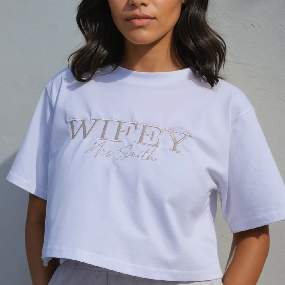 A female model modelling a honeymoon crop t shirt with WIFEY embroidered in statement text and Mrs Smith embroidered in cursive font