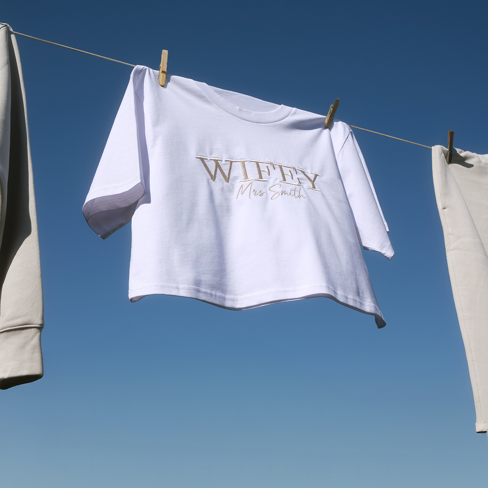 A crop t shirt that has WIFEY embroidered on it in statement text hanging on a washing line
