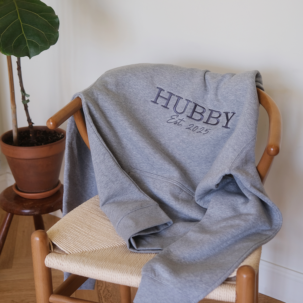 A hoodie that has HUBBY est 2025 embroidered on it laying on a chair