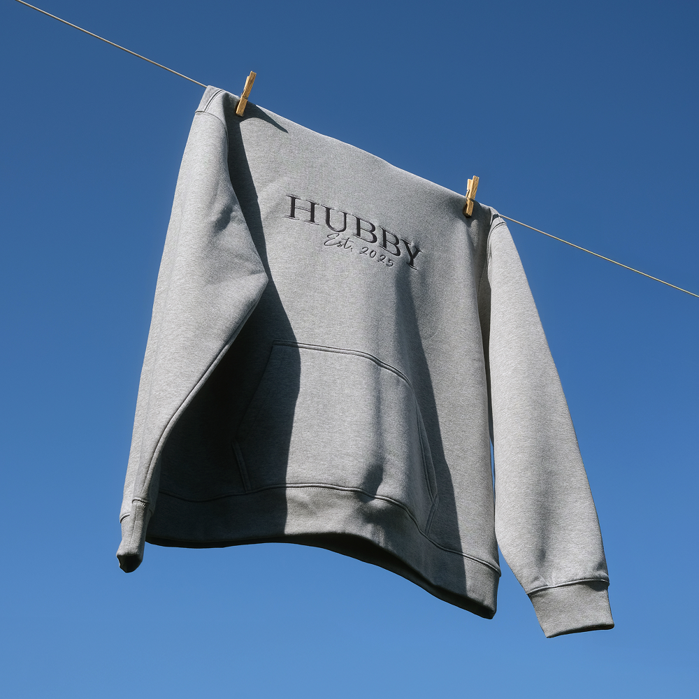 A luxe looking hoodie that has HUBBY est 2025 on it hanging on a washing line