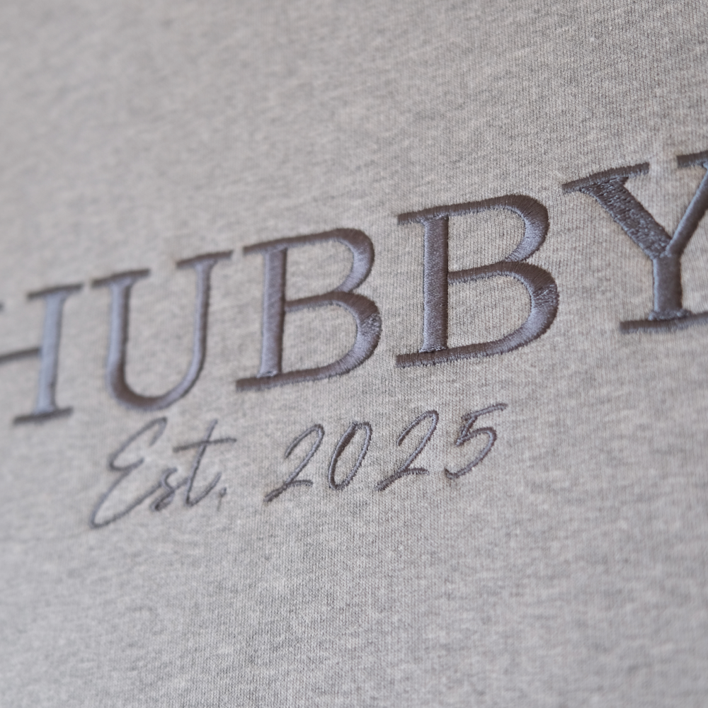 A luxe looking hoodie that has HUBBY est 2025 on it hanging on a washing line