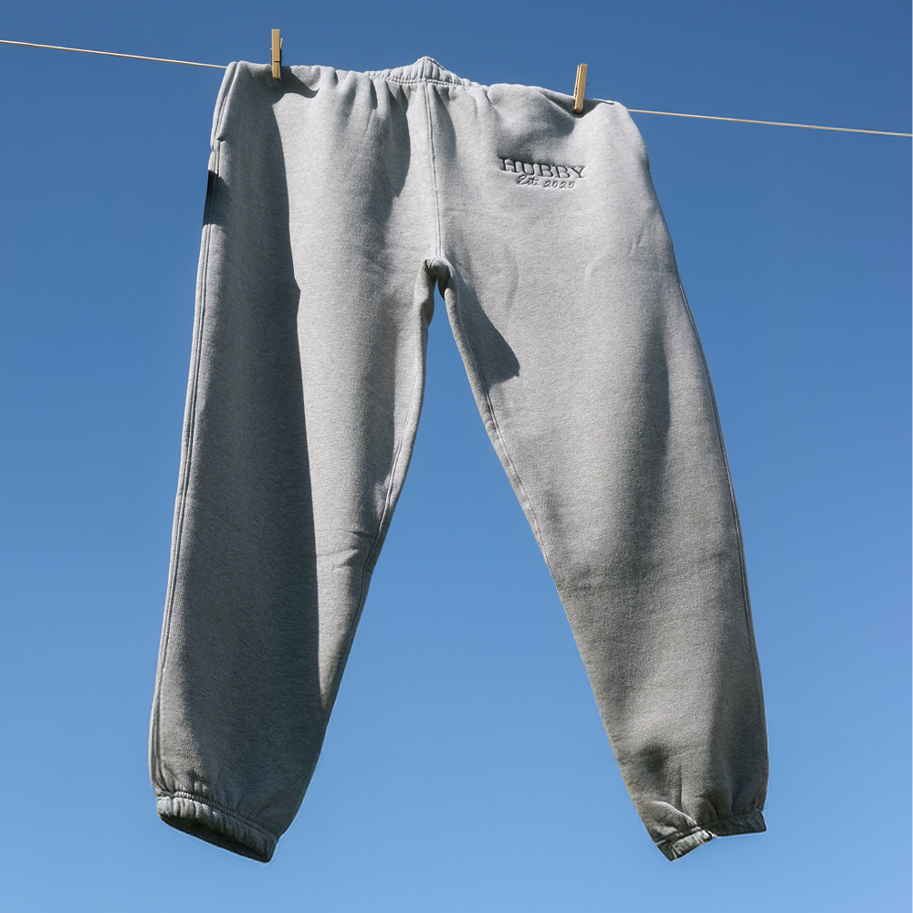 A pair of athletic heather coloured luxurious joggers embroidered with HUBBY est 2025 hanging on a washing line